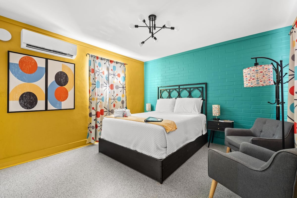 Een slaapkamer met een bed, een stoel, een airconditioner, een lamp en een muur met een geometrisch patroon.
