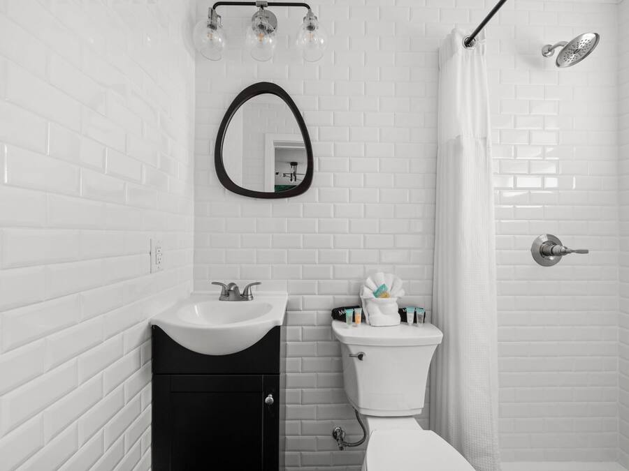 A bathroom with white tiled walls, a black cabinet, a sink, a toilet, a shower, and a mirror.