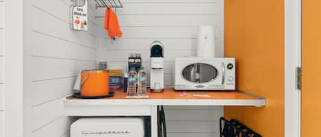 A kitchenette with a white refrigerator, a microwave, a kettle, and a coffee maker.
