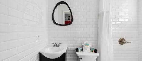 A bathroom with white tiled walls, a black cabinet, a white sink, a toilet, a mirror, and a shower curtain.