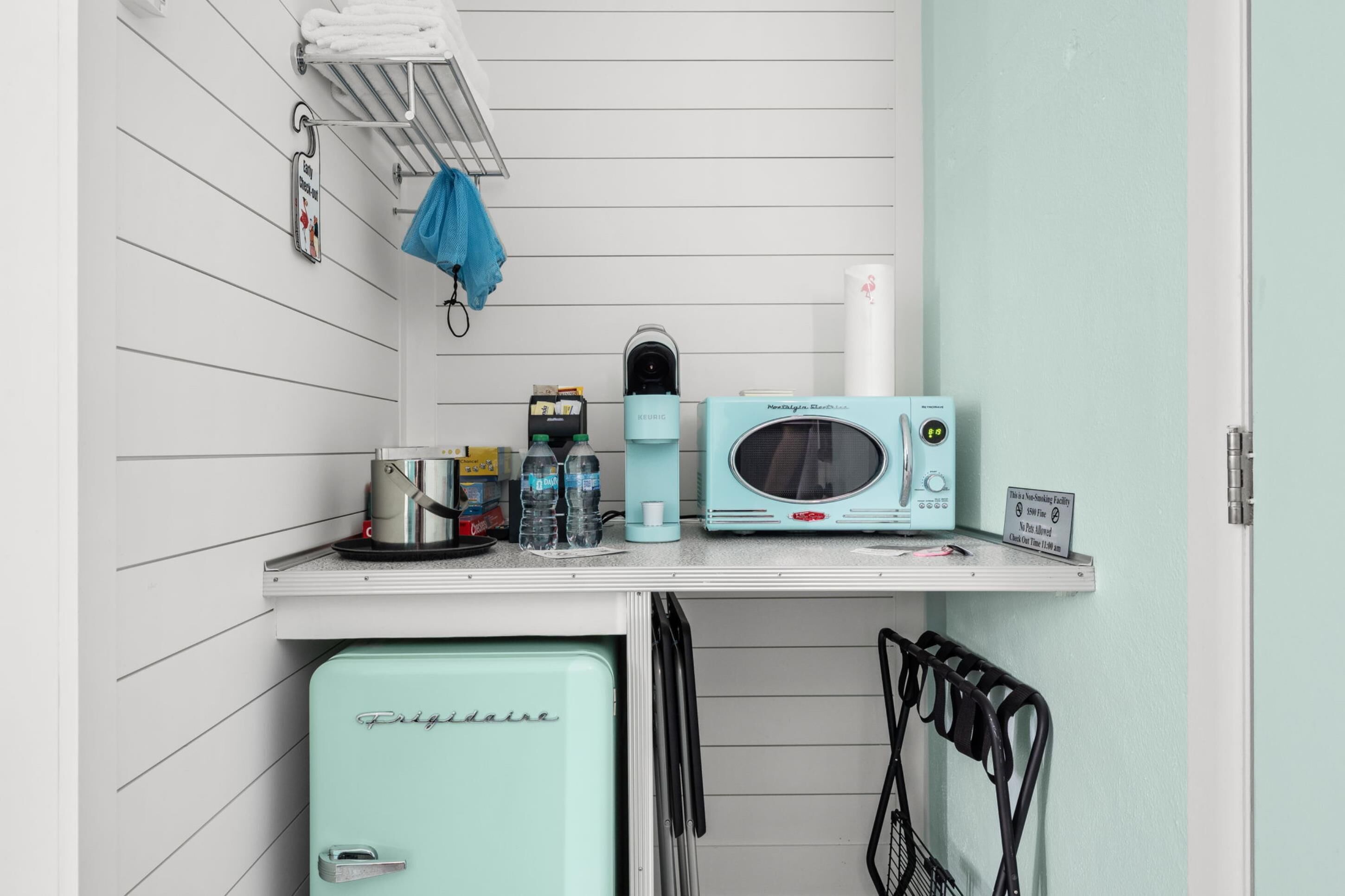 Una kitchenette compacta con un refrigerador antiguo, un microondas, una cafetera y un lavamanos pequeño.