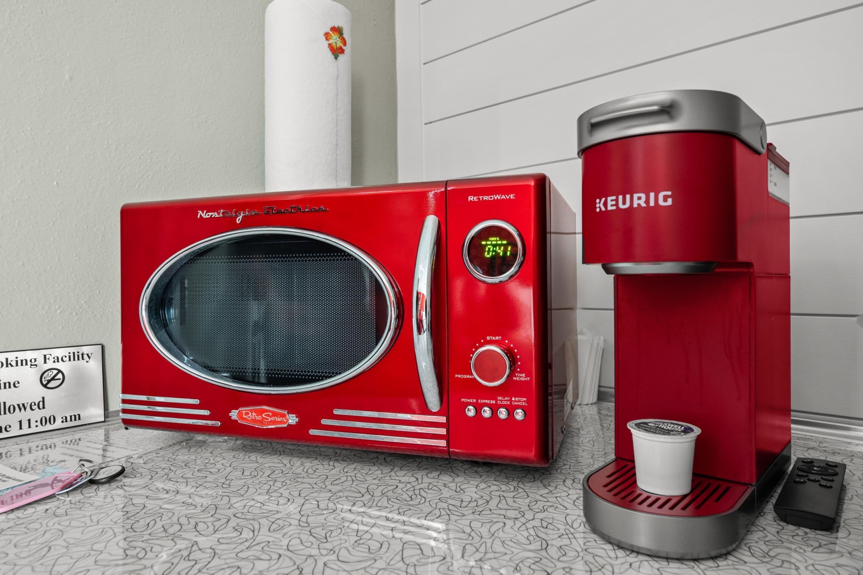 Een rode RetroWave magnetron en Keurig koffiezetapparaat staan op een patroon vloer, met een bordje dat aangeeft dat roken na 11:00 uur niet is toegestaan.