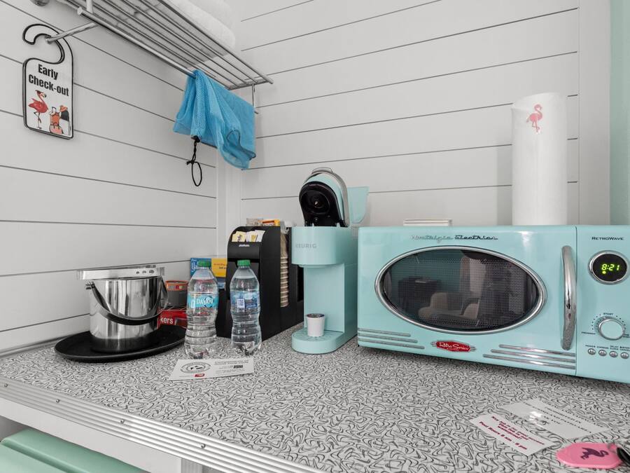 A kitchenette with a retro-style microwave, coffee maker, and kettle. There are water bottles and a coffee pod on the counter.