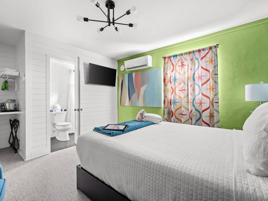 Una habitación de hotel con cama, escritorio, televisor, aire acondicionado y baño.