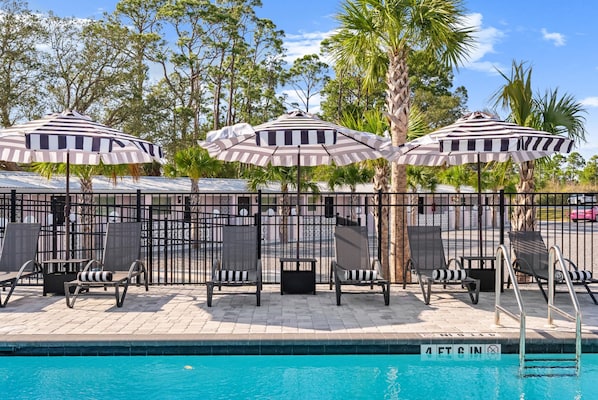 A poolside area with striped umbrellas, lounge chairs, and a fenced pool. - The Pink Flamingo Boutique Motel (Port St. Joe)