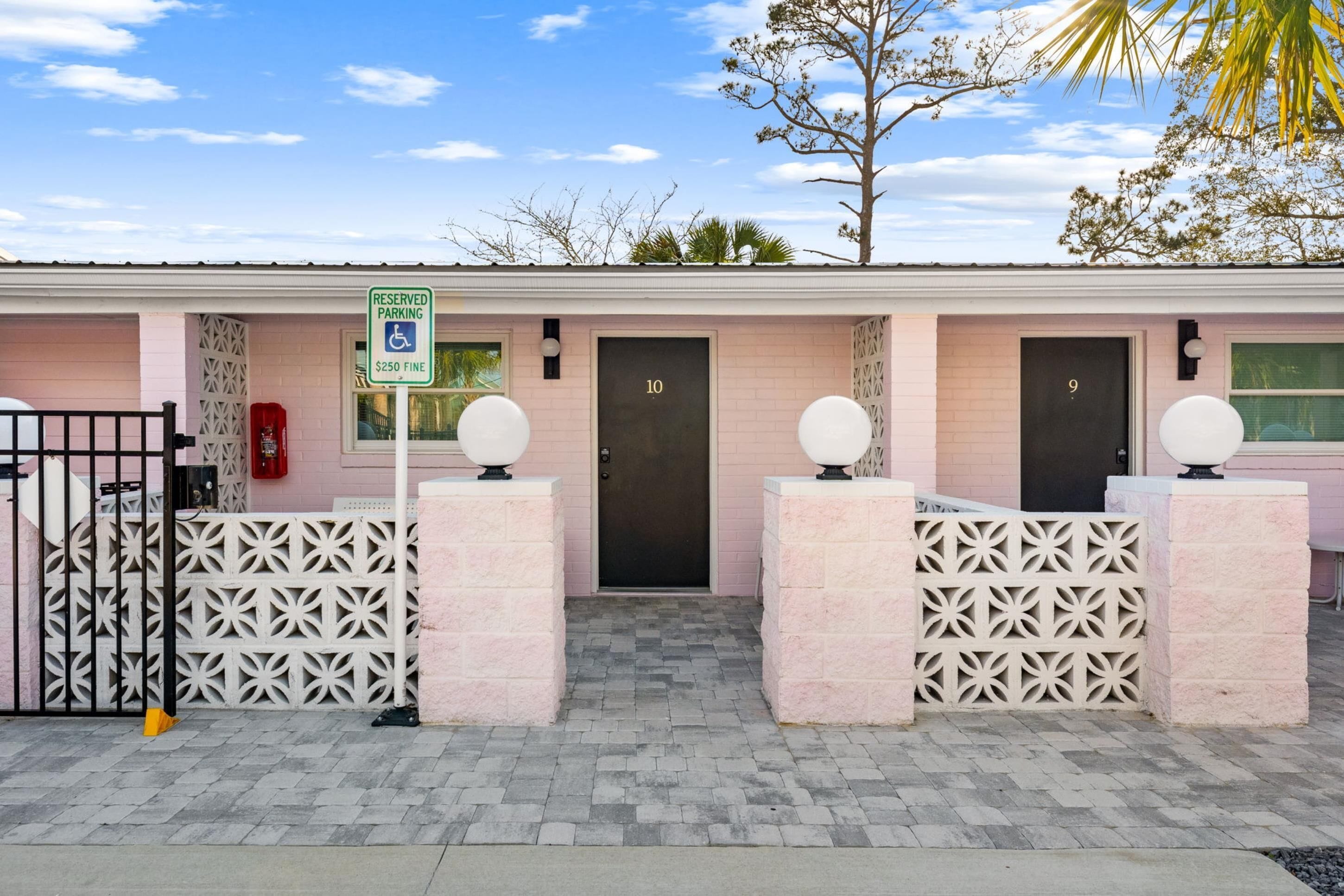 Un edificio rosa con puertas numeradas, un letrero de estacionamiento reservado y una entrada con portón.