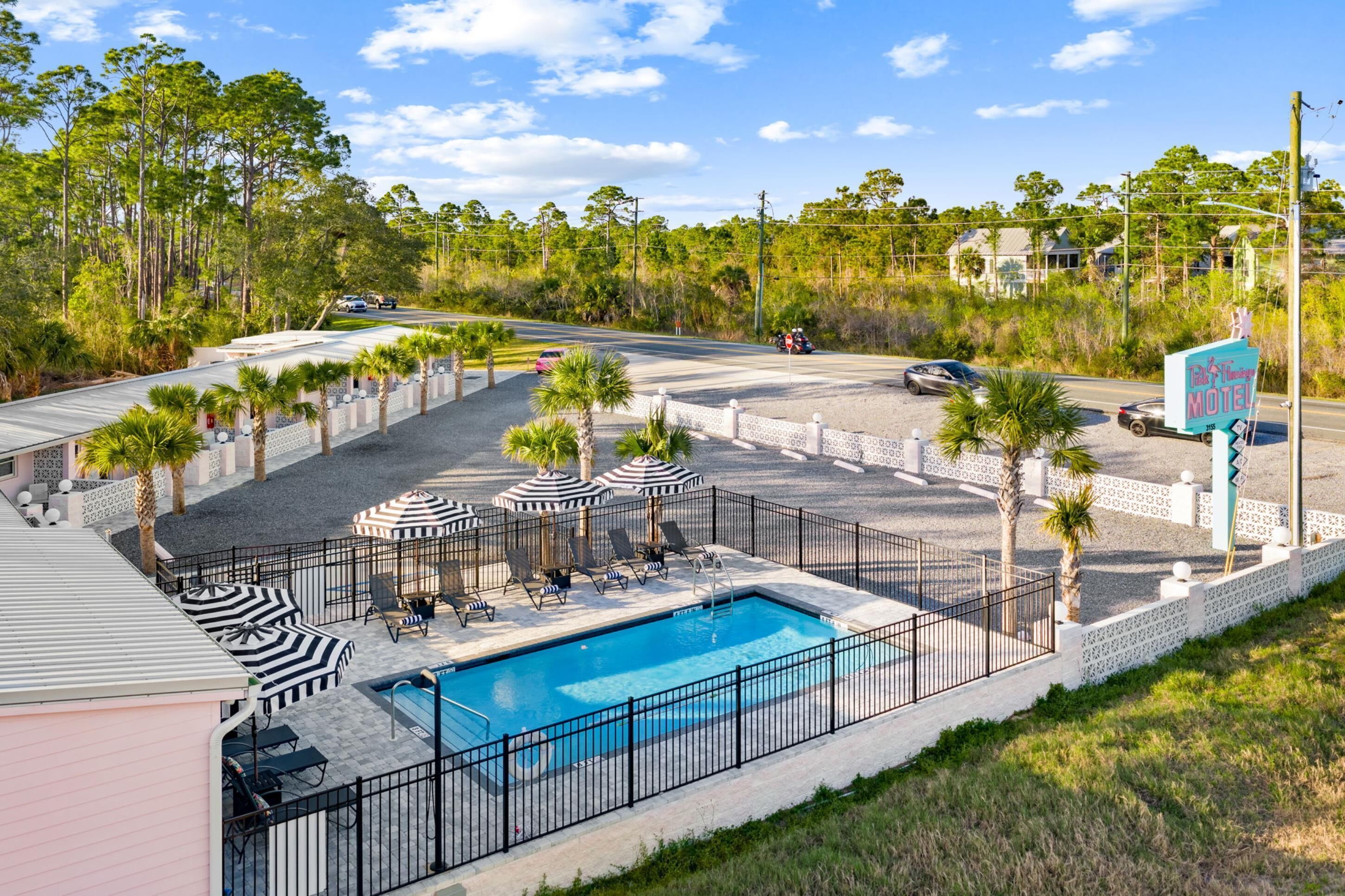 A pool area with lounge chairs and umbrellas, surrounded by a fence and palm trees.