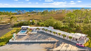 Ein Resort mit Pool, Blick auf den Strand und einem pinkfarbenen Auto vor der Fassade.