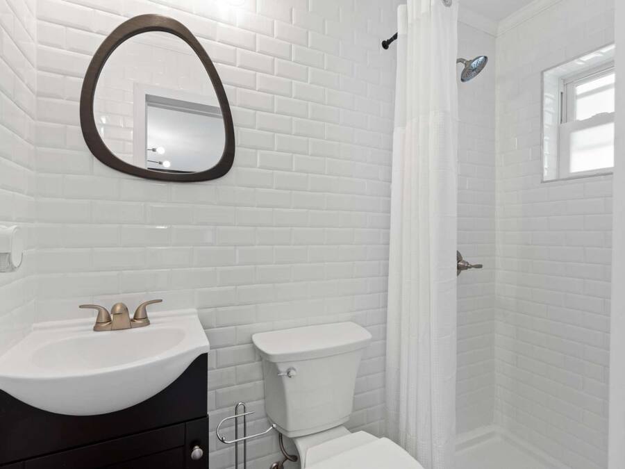Un baño con azulejos blancos tipo metro, un espejo redondo, un lavabo con grifo dorado y un inodoro.