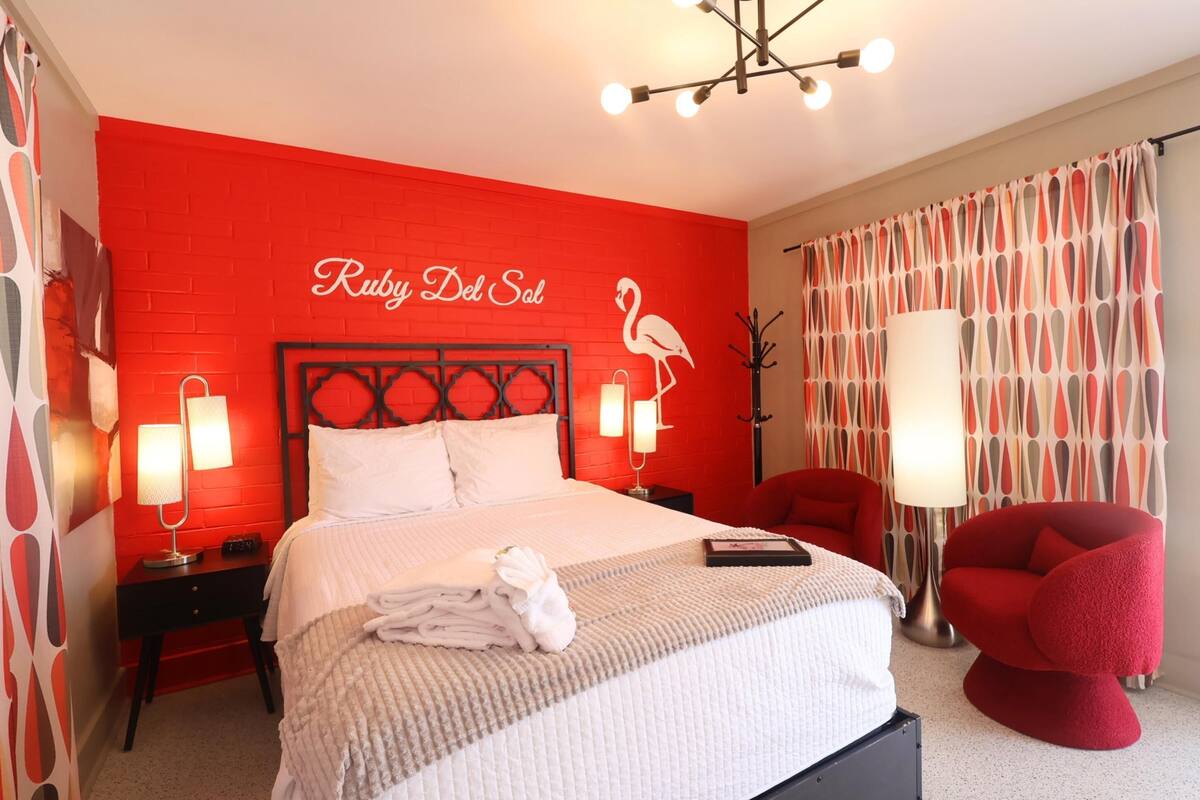 Een hotelkamer met een rode bakstenen muur, een bed met witte lakens, een rode stoel en een wandlamp.