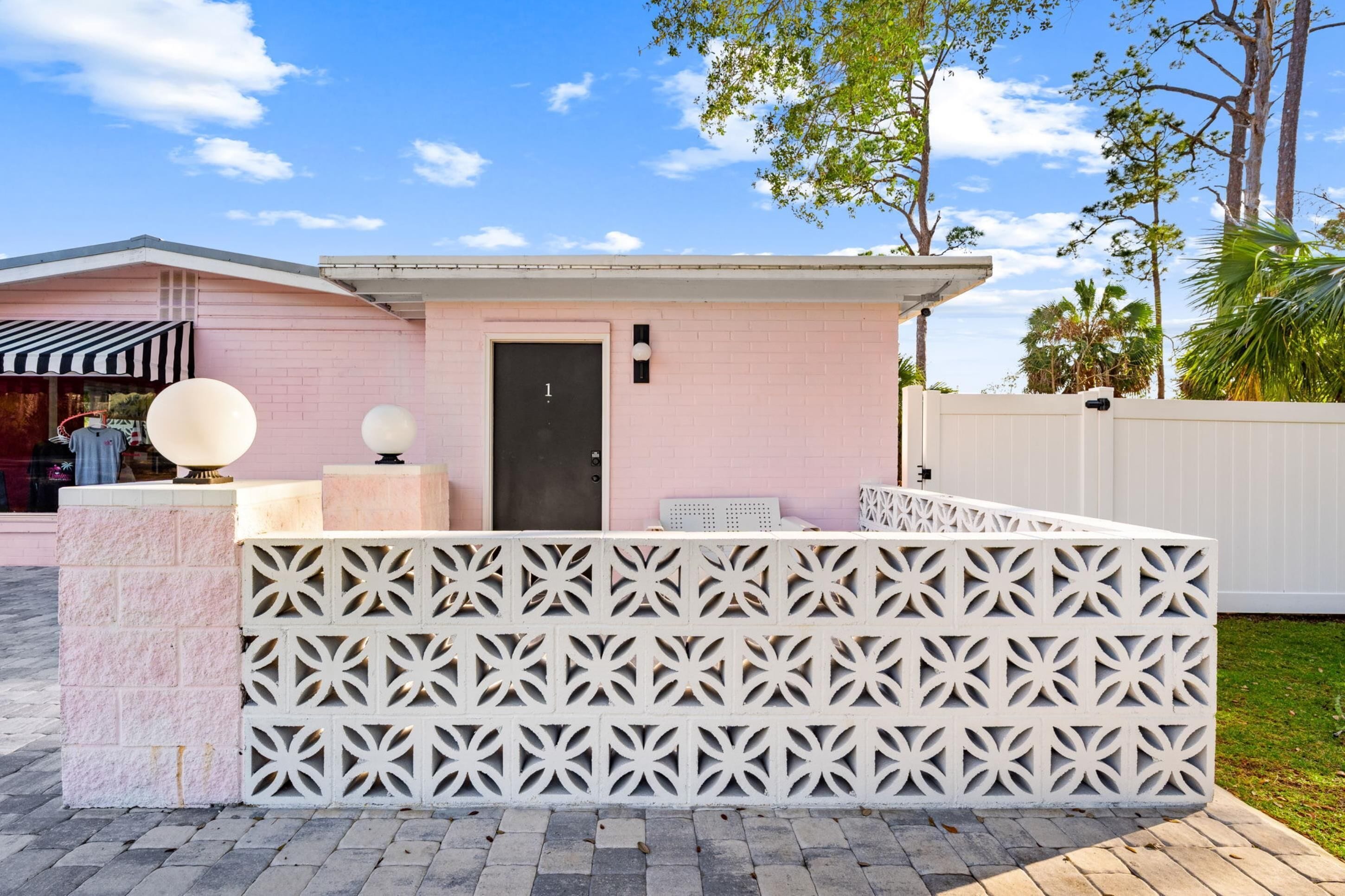 A pink building with a door marked "1", a white fence with a geometric pattern, and a small outdoor seating area with a round table and chairs.