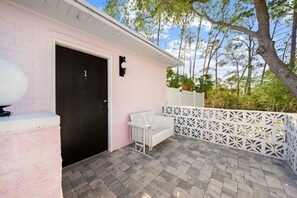 A pink building with a black door, a white bench, and a white fence with geometric patterns. - The Pink Flamingo Boutique Motel (Port St. Joe)