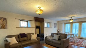 Ein geräumiges Wohnzimmer mit zwei Sofas, einem Couchtisch und einem Kamin. Es gibt Fenster und einen Deckenventilator.