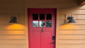Eine rote Tür mit einem kleinen Fenster darüber, beides von zwei Wandleuchten beleuchtet.
