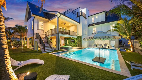 Une maison à deux étages avec une piscine, un espace salon extérieur et un balcon.