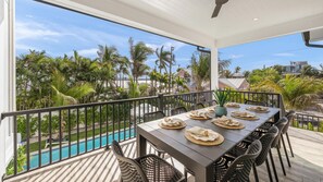 Un balcon avec une table dressée pour le dîner, donnant sur une piscine et des palmiers.
