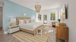 Une chambre à coucher comprenant un lit, des tables de chevet, une commode, un banc en bois, une coiffeuse, un miroir et un luminaire suspendu.