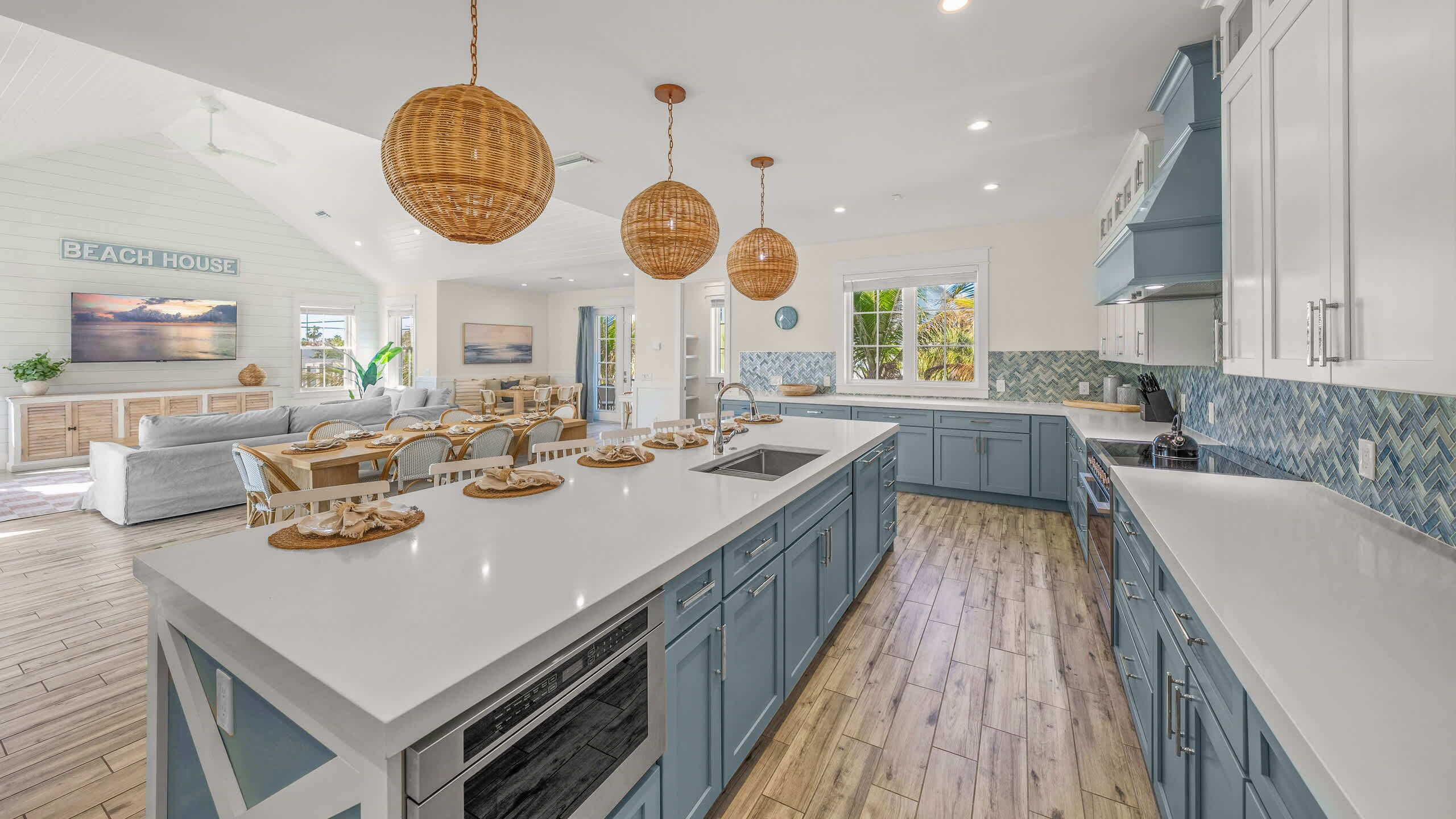 A spacious kitchen with a large island, blue cabinets, and hanging wicker pendant lights.
