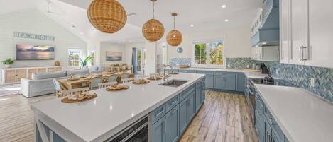 A spacious kitchen with a large island, blue cabinets, and hanging wicker pendant lights.