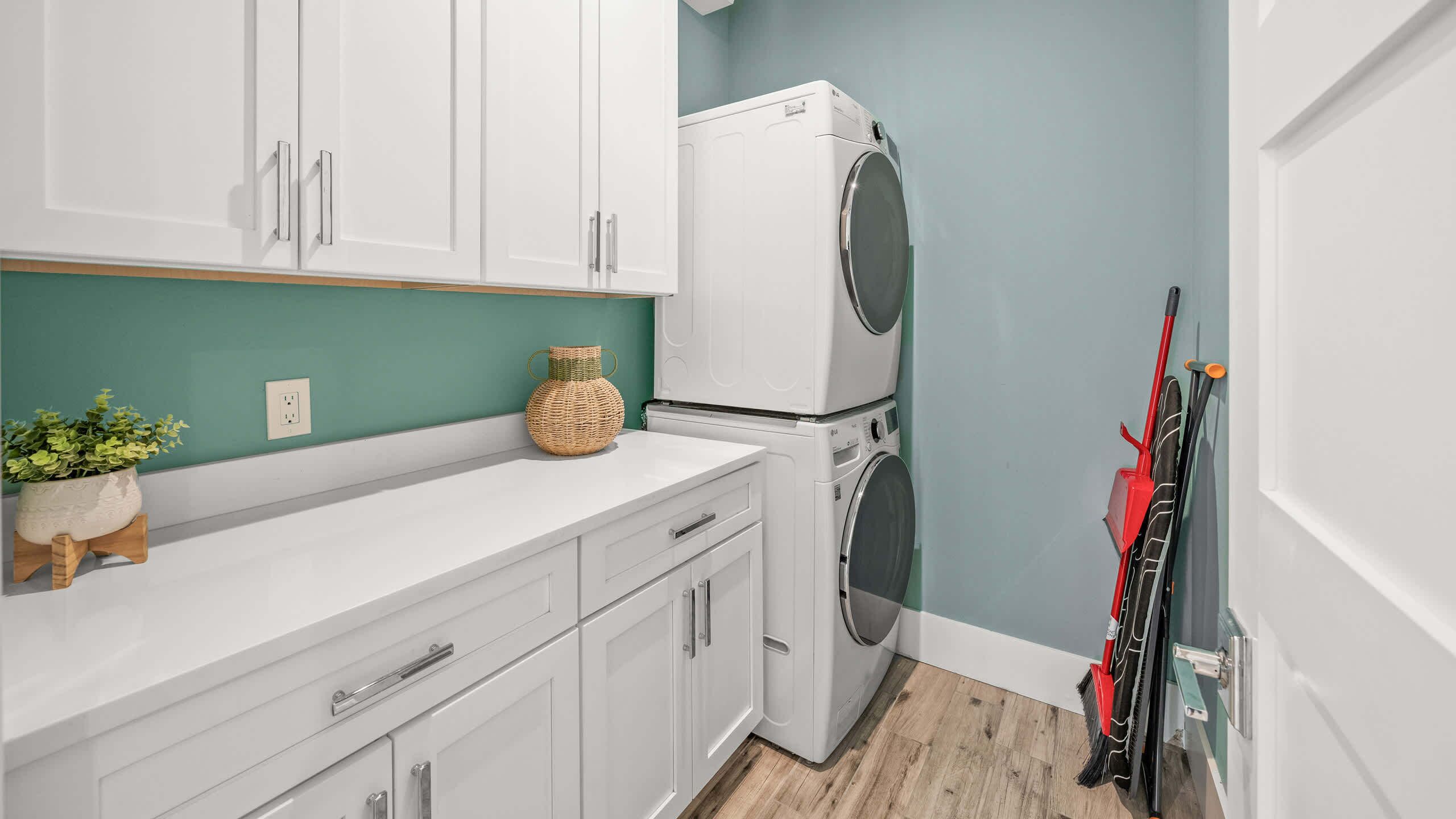 A laundry room with a washing machine, a drying machine, a sink, and a broom leaning against the wall.