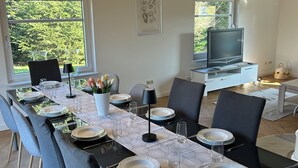 Ein Essbereich mit einem langen Tisch, gedeckt für sechs Personen, einem Fernseher und einem gerahmten Pflanzenprint an der Wand.