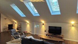 Ein modernes Wohnzimmer mit schrägen Decken, Oberlichtern, einem Flachbildfernseher, einer Couch und einem Esstisch.