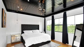 Een moderne slaapkamer met een groot bed, een decoratieve plafondlamp en uitzicht op het buitengebied door grote ramen.