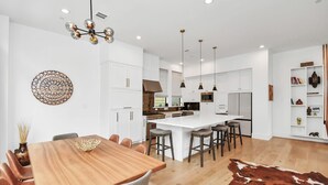 Een moderne keuken met witte kasten, een centraal eiland met barstoelen, hanglampen en een koeienhuidtapijt op de vloer.
