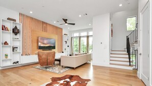 Een moderne woonkamer met een houten vloer, een grote leren bank, een flatscreen-tv en een plafondventilator.