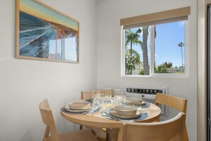 A dining area with a round table, chairs, and a window with a view of palm trees. - Pacific Tides 7 - Modern Studio In Pacific Beach w/ AC + Parking - Walk to Beach (San Diego)