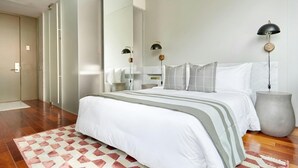 A modern bedroom with a large bed, a nightstand, a wall-mounted lamp, and a large mirror. - The Slate Hotel  (Toronto)