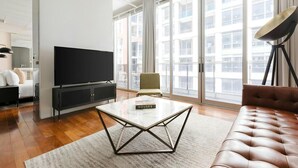 A modern living room with a large TV, a sofa, a chair, and a floor lamp. - The Slate Hotel  (Toronto)