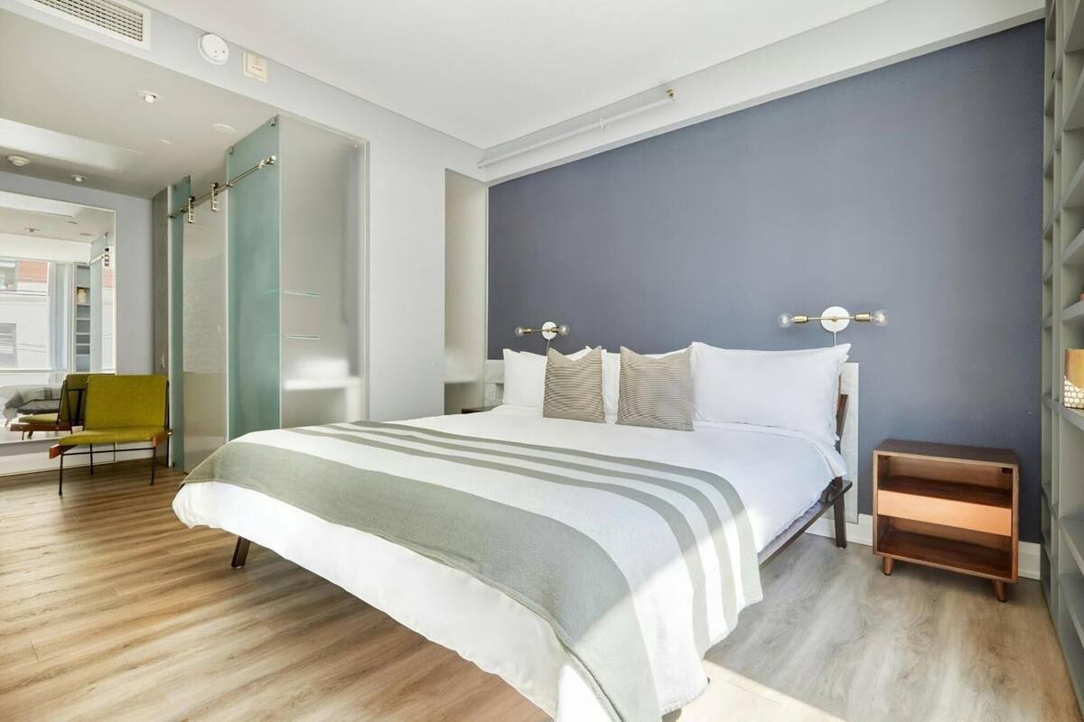A modern bedroom with a large bed, a bedside table, a chair, and a wardrobe.