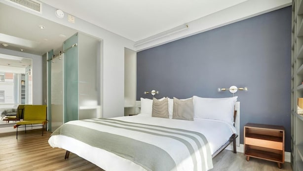 A modern bedroom with a large bed, a bedside table, a chair, and a wardrobe. - The Slate Hotel  (Toronto)