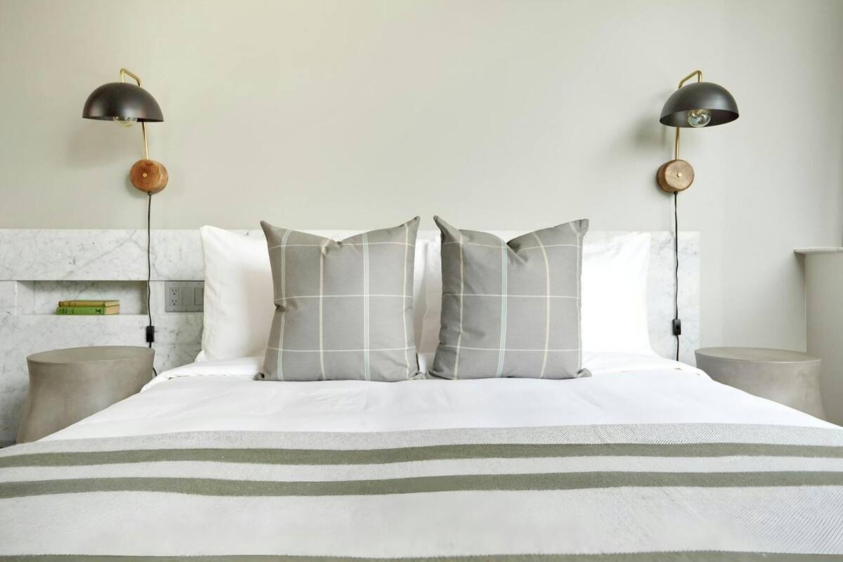 A neatly made bed with a striped bedspread, two bedside lamps with wooden bases, and a marble wall behind the bed.
