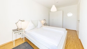 Un dormitorio con una cama grande, una mesita de noche con lámpara, un armario y un espejo redondo en la pared.