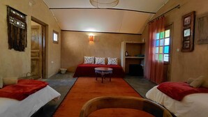 Een gezellige kamer met een bed, twee stoelen, een klein tafeltje en een raam met gordijnen.