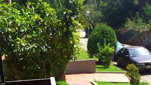 A balcony with a wooden chair, a paved pathway, and a car parked in the background. - A Peaceful Riverside Escape Just Minutes from Porto (São Cosme)
