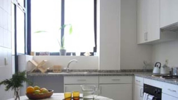 A modern kitchen with white cabinets, a dining table with a white tablecloth, and a window with a plant. - A Peaceful Riverside Escape Just Minutes from Porto (São Cosme)