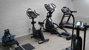 Ein Fitnessstudio mit verschiedenen Trainingsgeräten, darunter ein Rudergerät, ein Crosstrainer und ein Laufband.