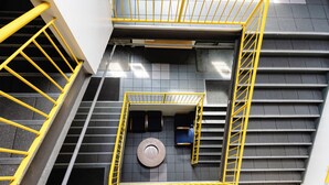 Eine mehrgeschossige Treppenhalle mit gelben Handläufen, einer Sitzgelegenheit in Form eines Kreises und einer kleinen, abgeschlossenen Nische mit einem Sessel.