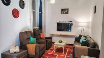 Uma sala de estar com dois sofás, uma mesa de centro, uma televisão e uma janela com cortinas.