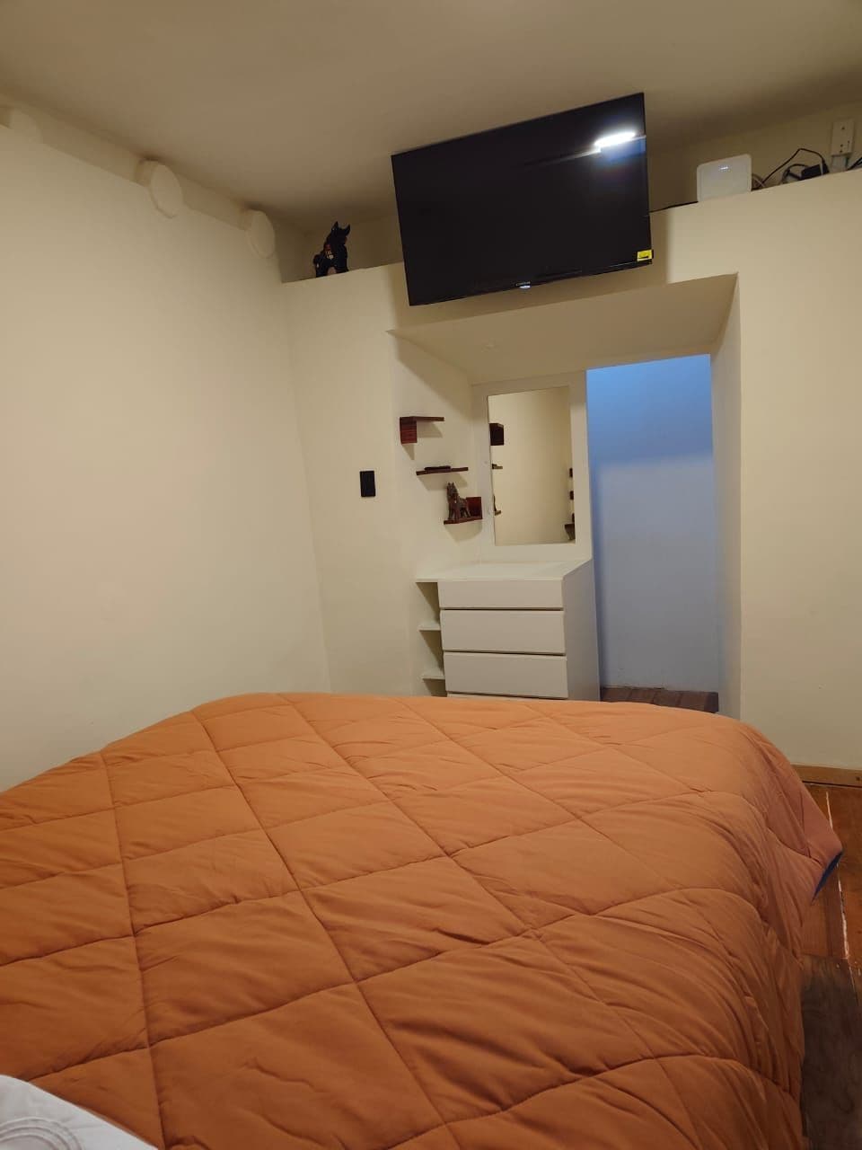 A bedroom with a bed, a television mounted on the wall, a dresser, and a mirror.