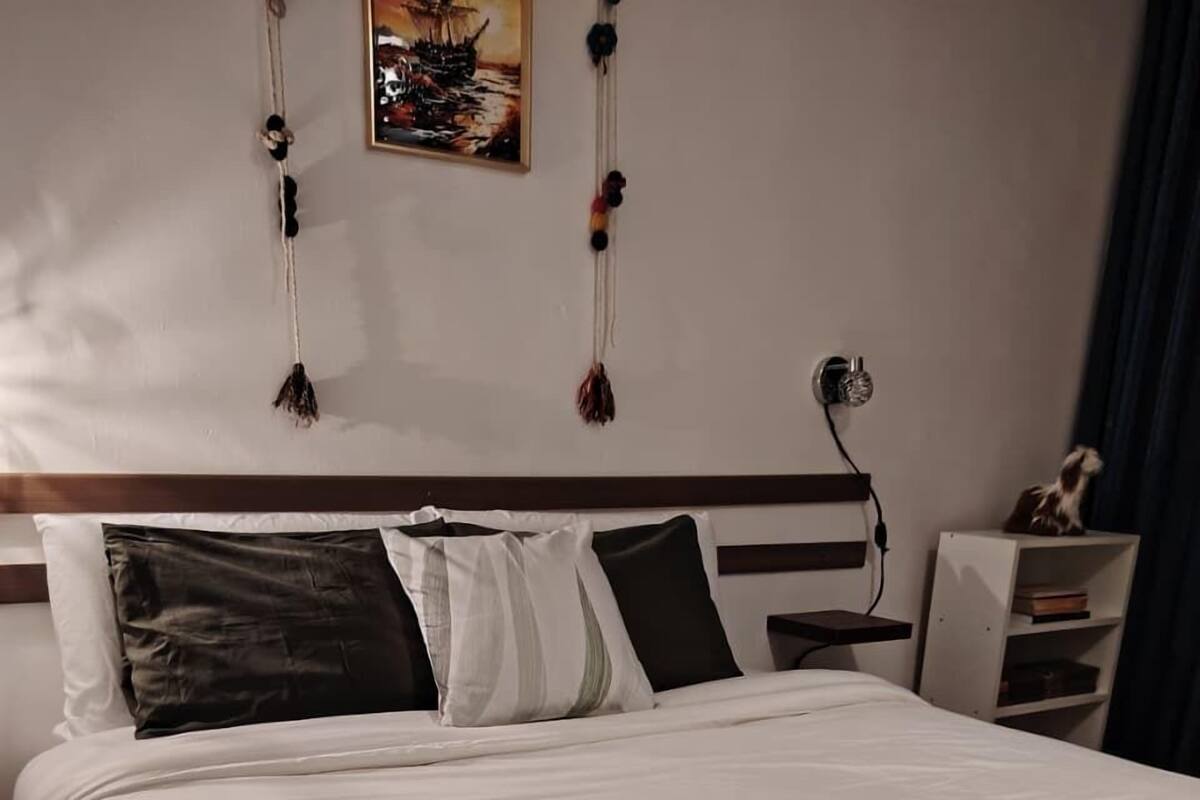 A neatly made bed with white linens, a dark throw blanket, and a headboard with a wooden finish.
