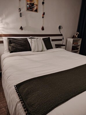 A neatly made bed with white linens, a dark throw blanket, and a headboard with a wooden finish. - KANTIQ House (Cusco)