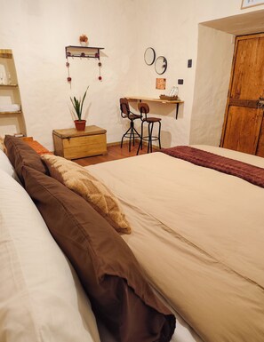 A bedroom with a bed, a wooden chest, a desk with two chairs, a potted plant, and a wardrobe. - KANTIQ House (Cusco)