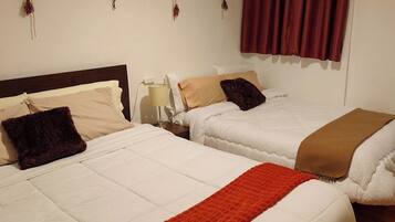 Two beds with white bedding and a red throw blanket, a nightstand with a lamp, and a painting on the wall.