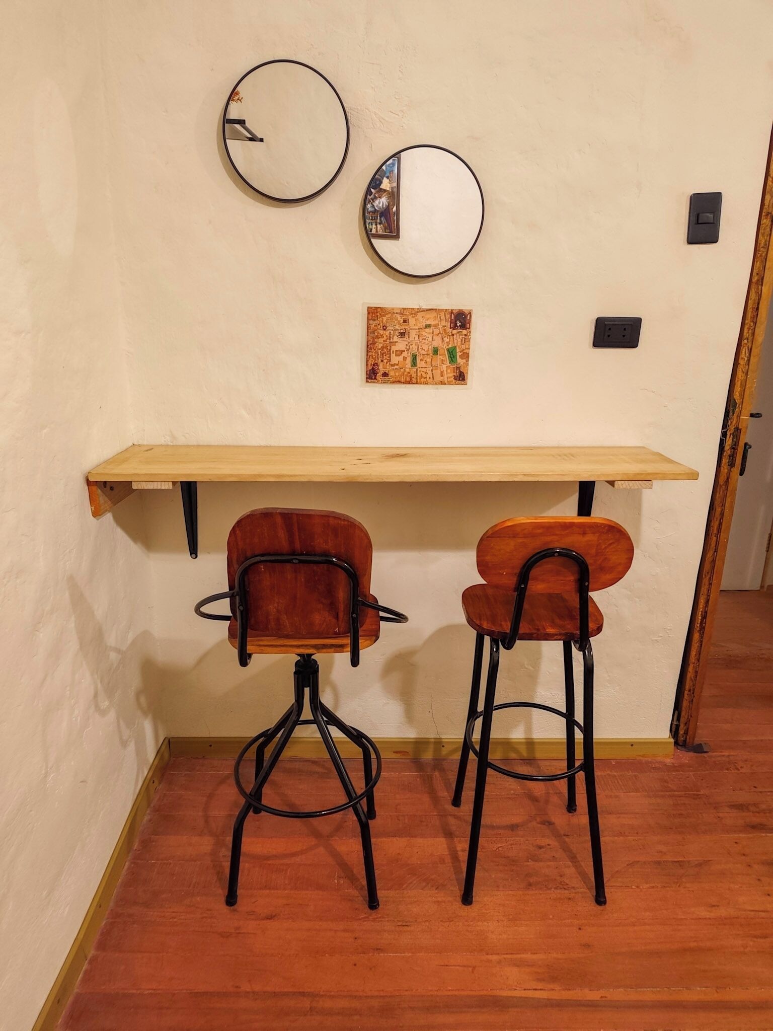 A room with a wooden desk, two chairs, two wall-mounted mirrors, and a map artwork.