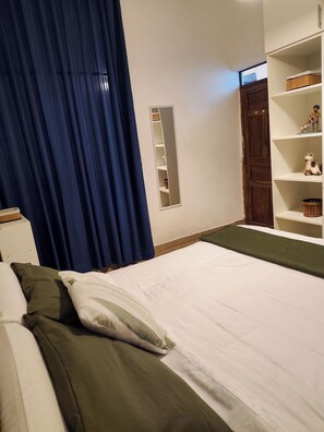 A bedroom with a bed, a wardrobe, a mirror, and a shelf with figurines. - KANTIQ House (Cusco)