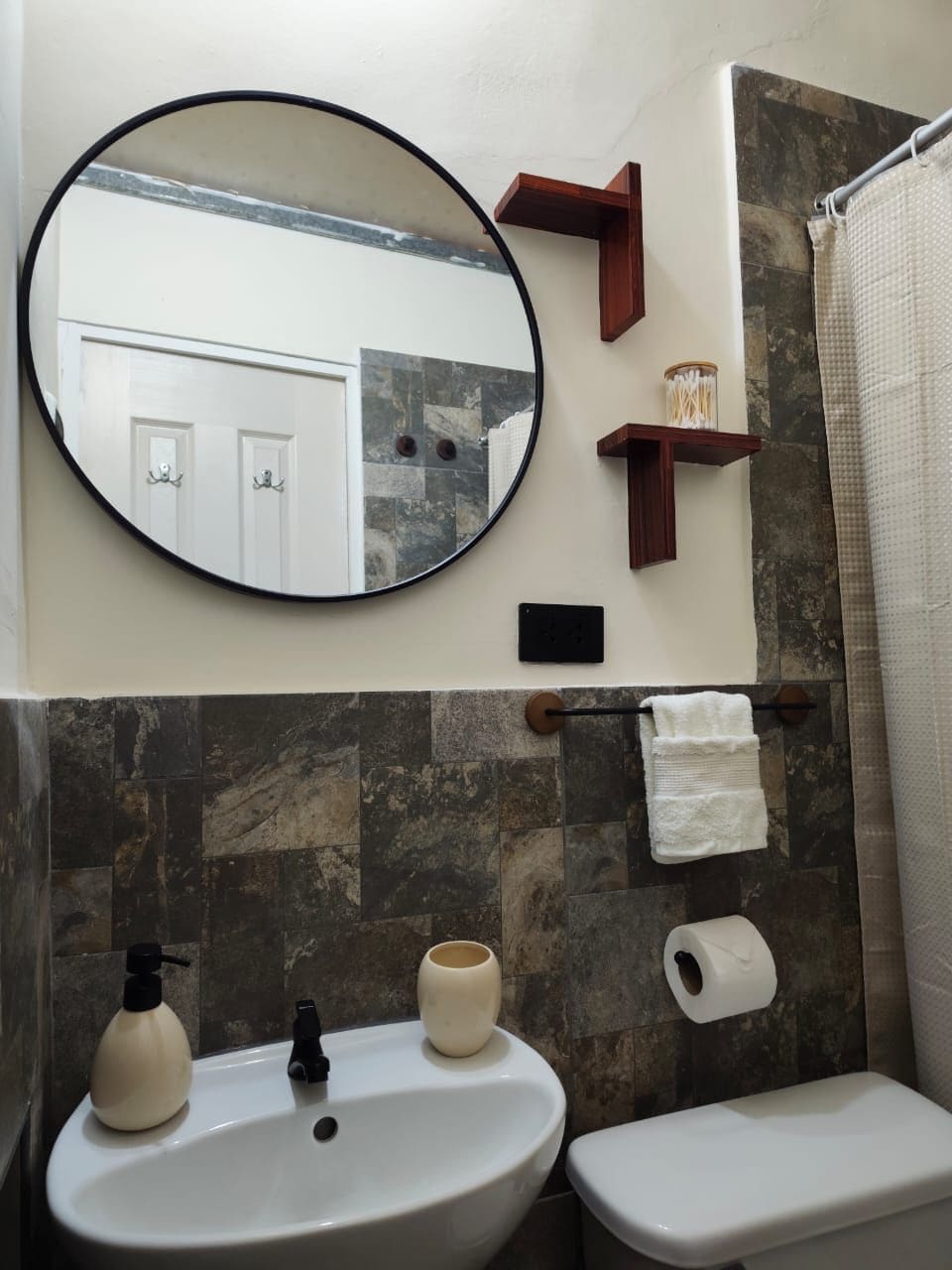 A bathroom with a round mirror, a sink, a toilet, and a shower curtain.